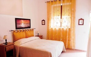 Une chambre à coucher avec un lit, deux tables de chevet, une commode, un tableau accroché au mur et une fenêtre avec des rideaux jaunes.