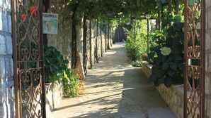 A stone pathway leading through a vine-covered archway, flanked by metal gates and stone walls. - B&B Il Grappolo (Anacapri)