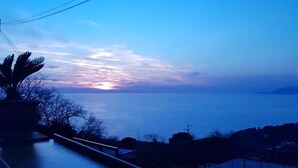 A coastal road with a sunset view, a palm tree, and distant landforms. - B&B Il Grappolo (Anacapri)