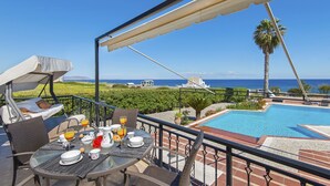 A dining area with a table set for breakfast, overlooking a swimming pool and the sea.