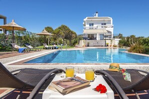 A poolside view with lounge chairs, a book, and two glasses of orange juice on a table.