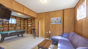 A room with a pool table, a sofa, a bicycle, and wooden paneling.