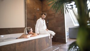 A modern bathroom with a large bathtub, wooden walls, and a window providing natural light. - Landhotel Weihermühle (Herschberg)