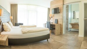 A modern hotel room with a curved bed, a desk, a television, and a bathroom visible through an open door. - Landhotel Weihermühle (Herschberg)