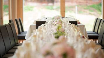 A dining table set with glassware and a floral centerpiece, surrounded by black upholstered chairs.