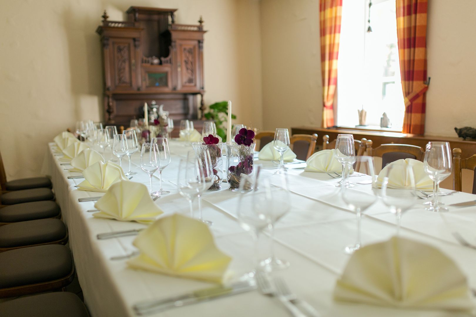 Mesa de jantar comprida posta para uma refeição formal, com toalhas brancas, copos e guardanapos amarelos.