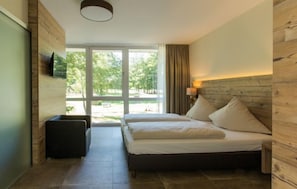 Een slaapkamer met een bed, een aan de muur bevestigde televisie en een raam met gordijnen.