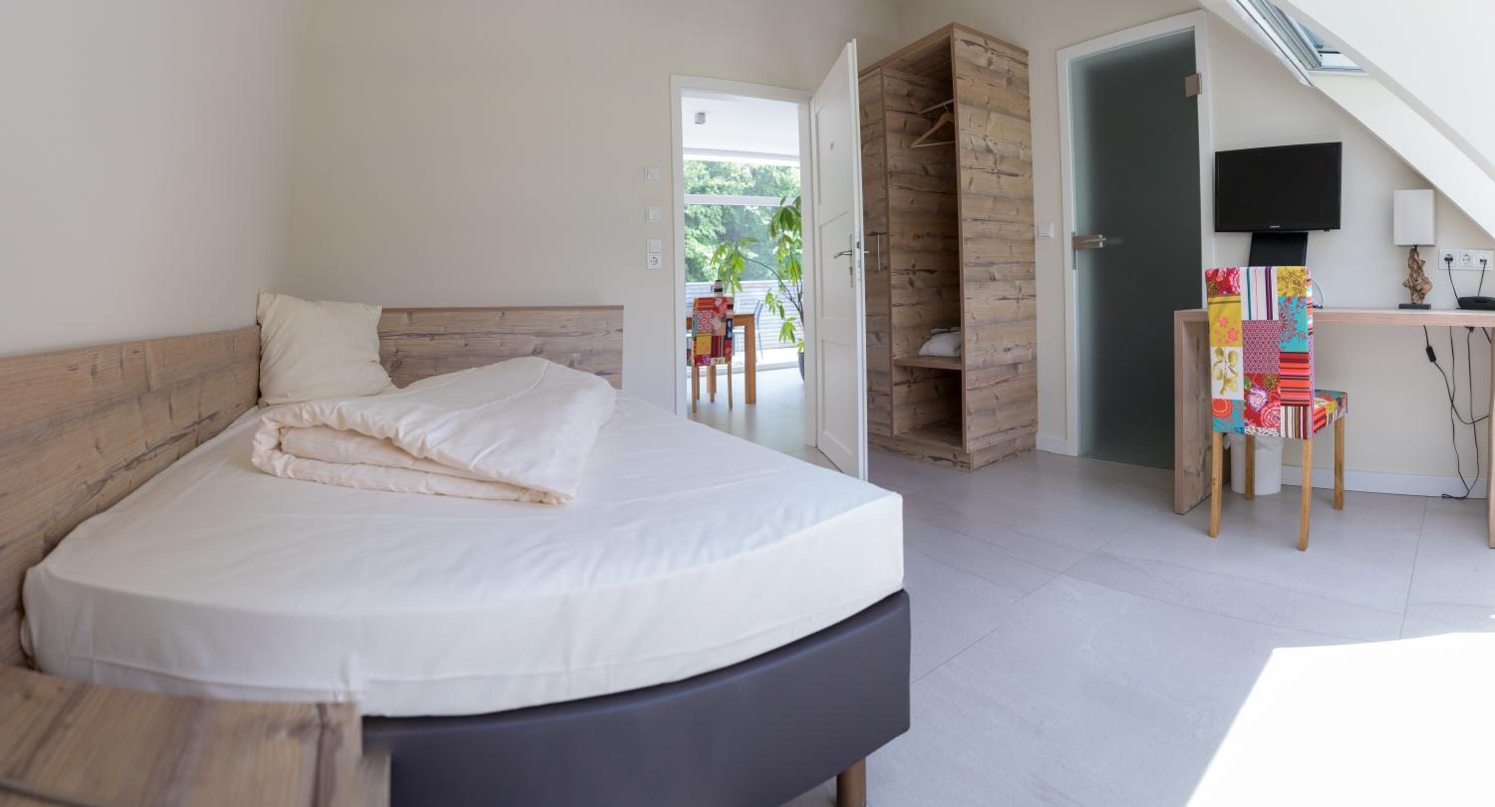A bedroom with a bed, a desk with a TV, and a wooden wardrobe.