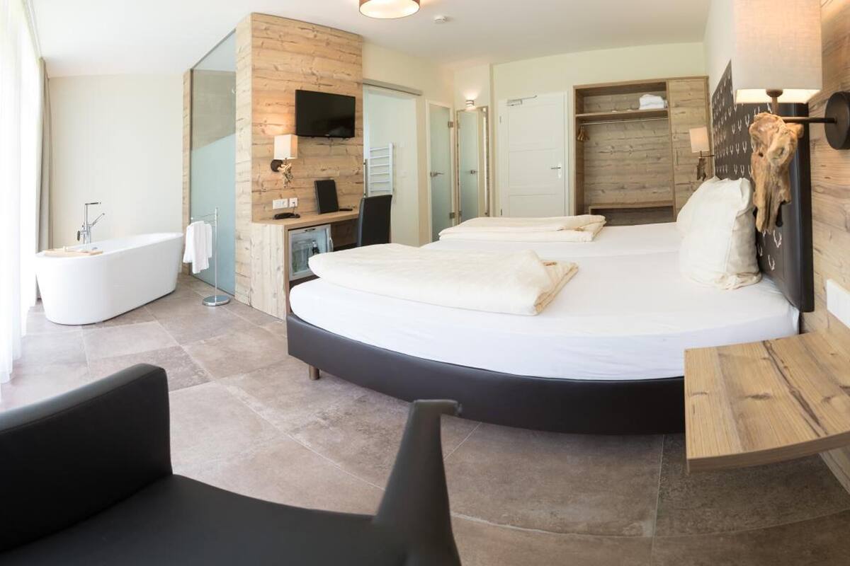 A modern hotel room with a large bed, a sitting area, a bathtub, and a wooden wall.