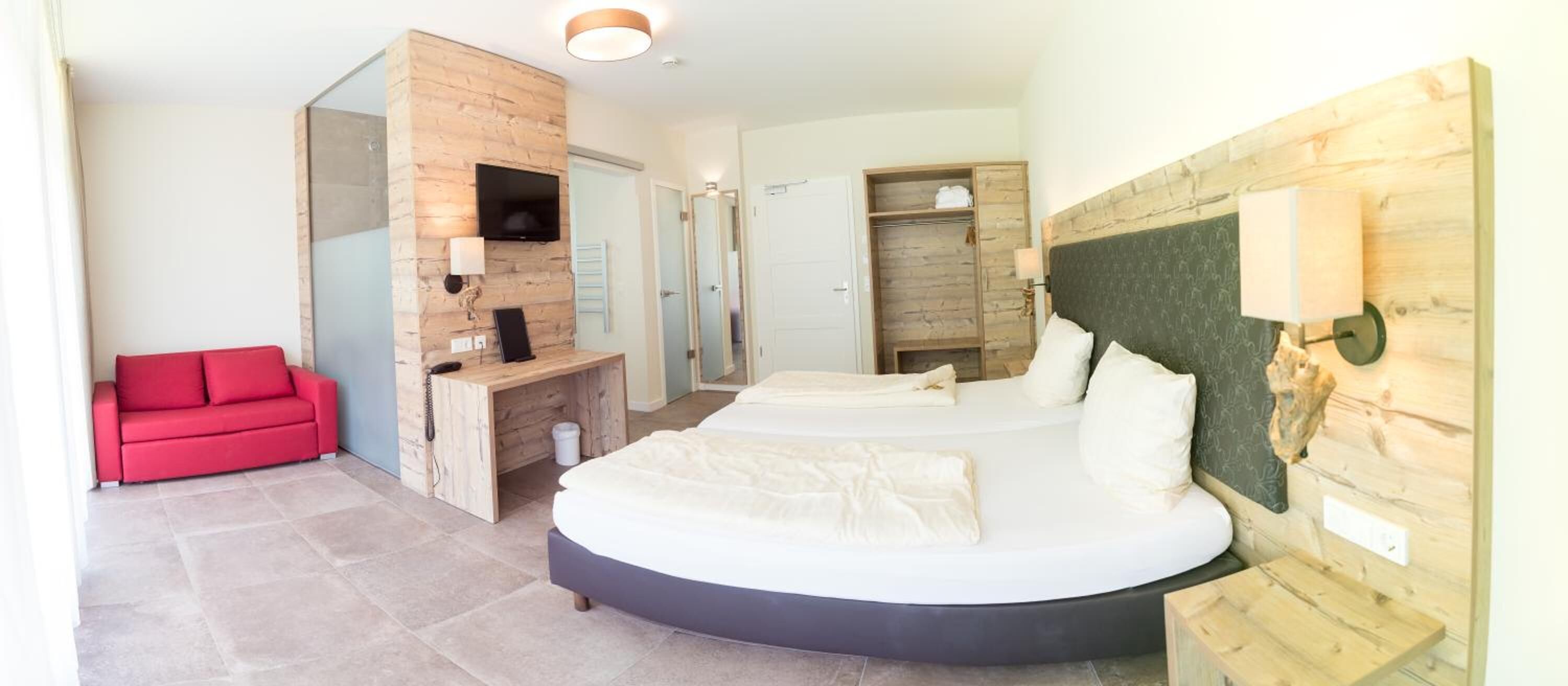 Um quarto moderno com uma cama curvada, um sofá vermelho, uma escrivaninha de madeira e um closet espaçoso.