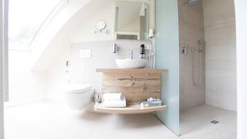 Ein modernes Badezimmer mit Dachfenster, einem weißen Waschbecken, einer Holz-Kommode, einer Dusche und einer Toilette.