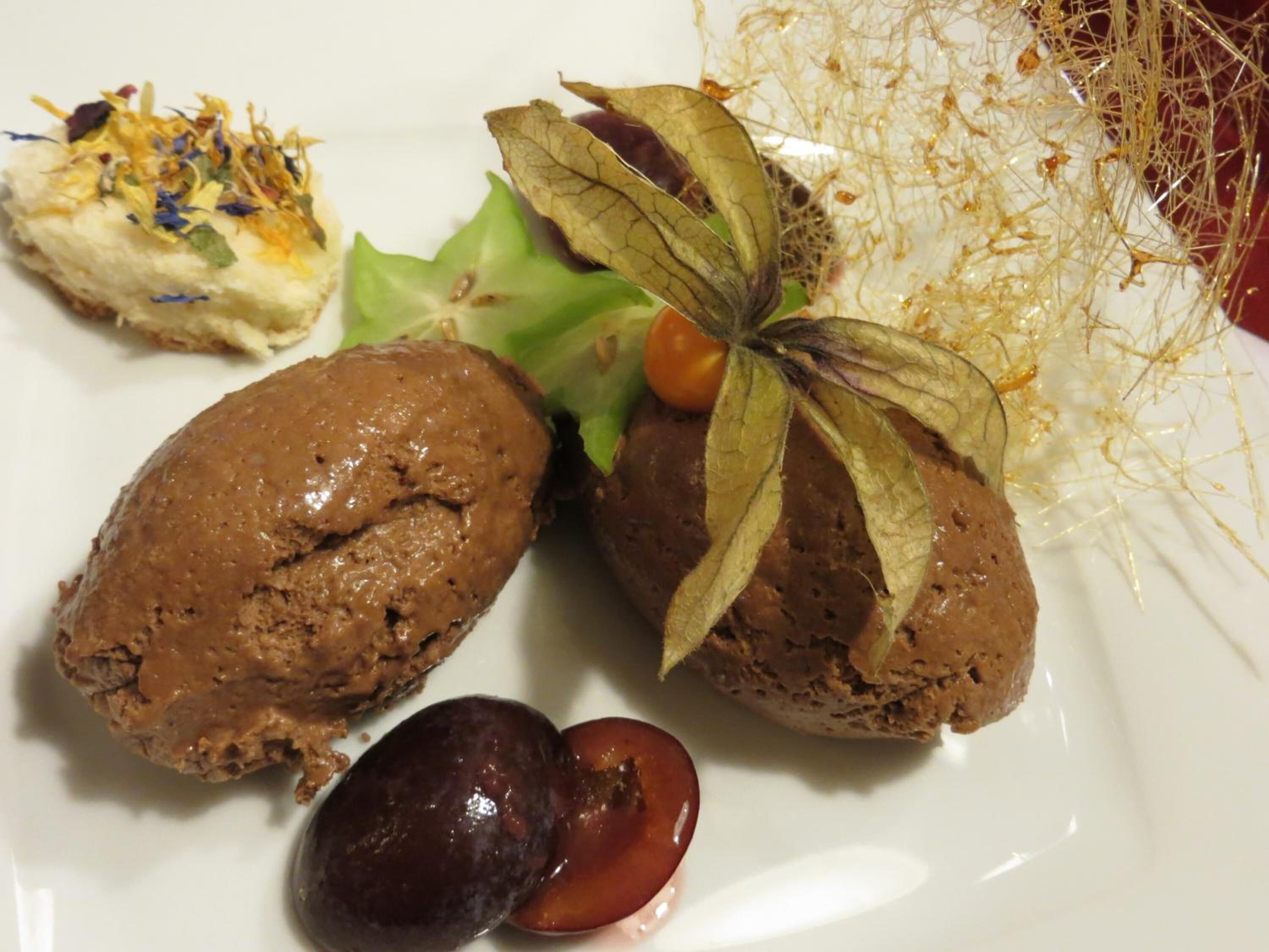 Un plato con dos postres de chocolate, una cereza y algunos detalles decorativos.