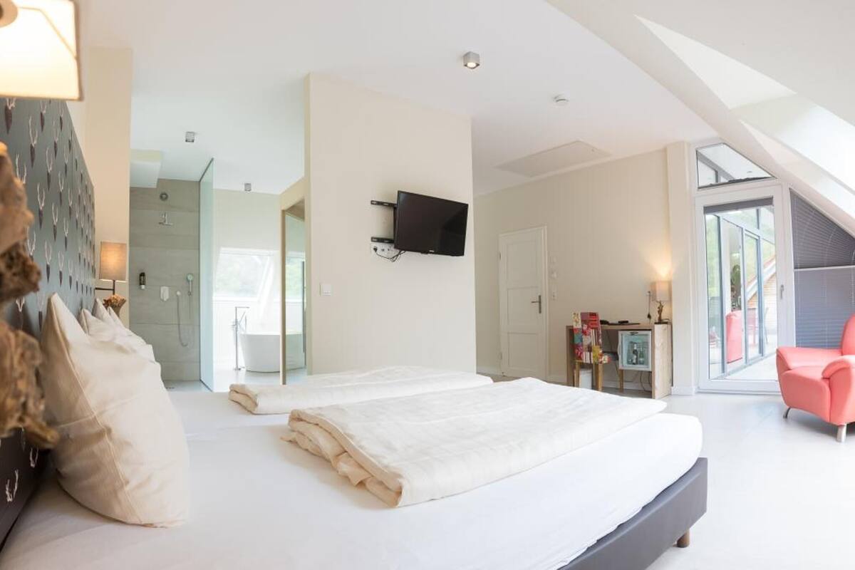 A modern bedroom with a large bed, a pink armchair, a mounted TV, and a skylight.