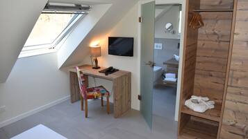 Una habitación moderna con techo inclinado, un escritorio con silla, un televisor y un armario de madera con espejo.