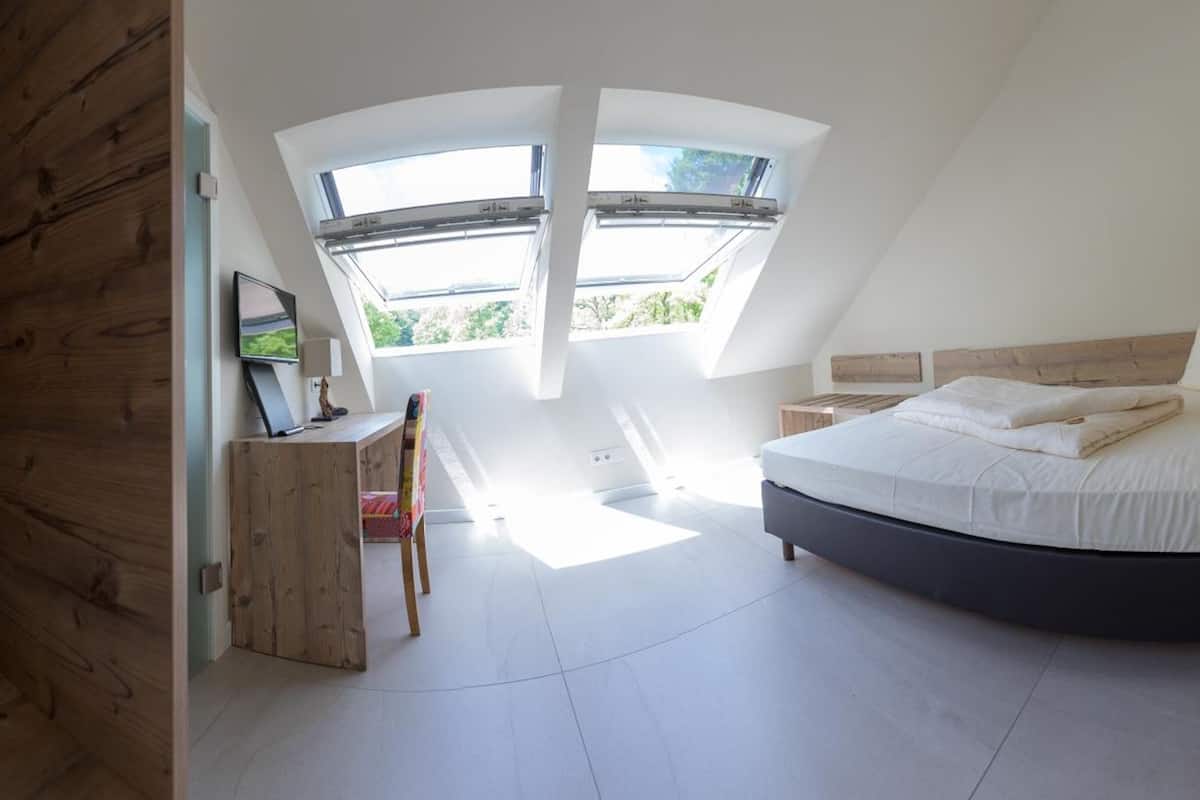 A bedroom with a curved bed, skylights, a desk, and a chair.