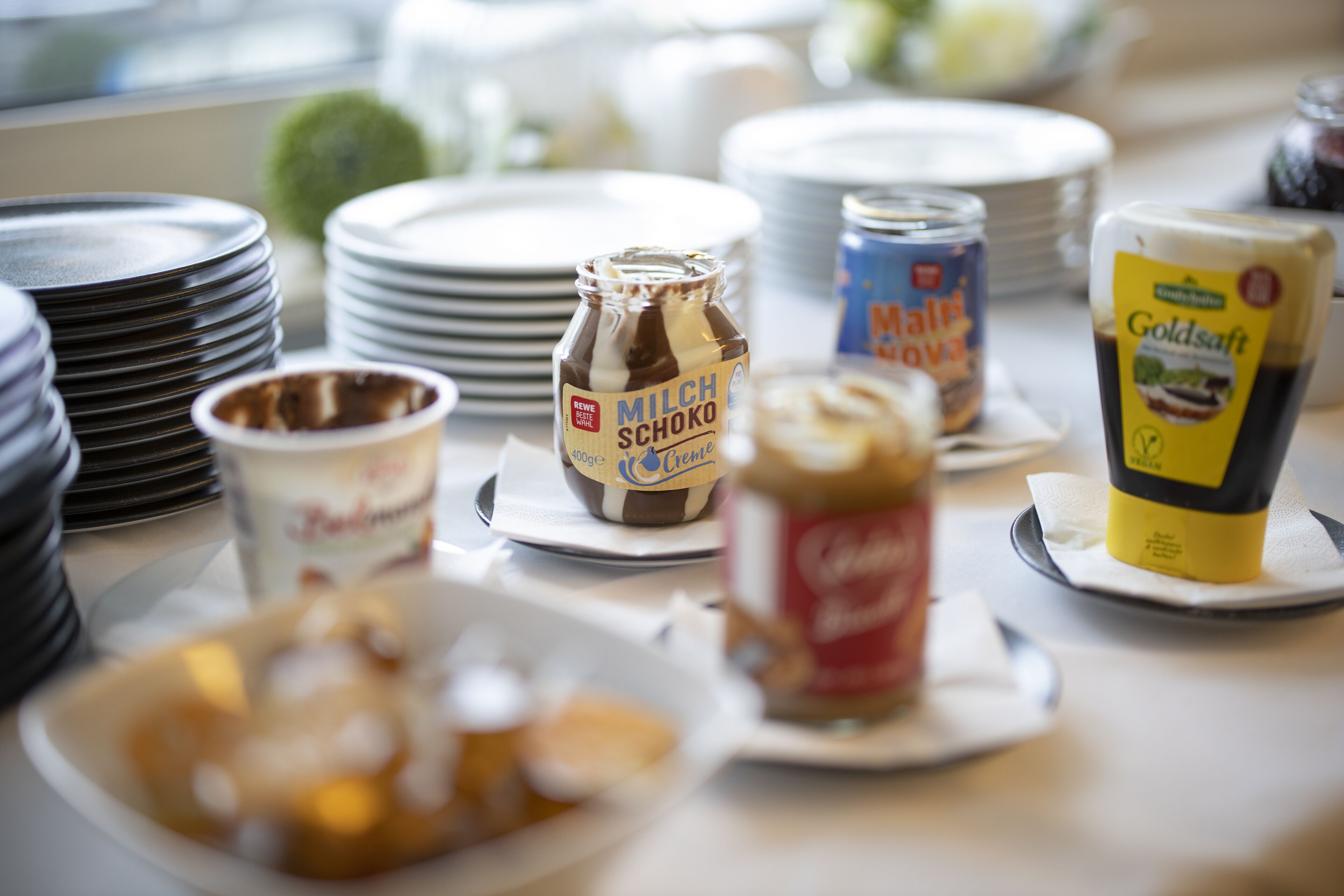 A buffet table with various food items and condiments, including a bottle of Milch Schoko, a jar of mustard, and a container of Goldsauf.