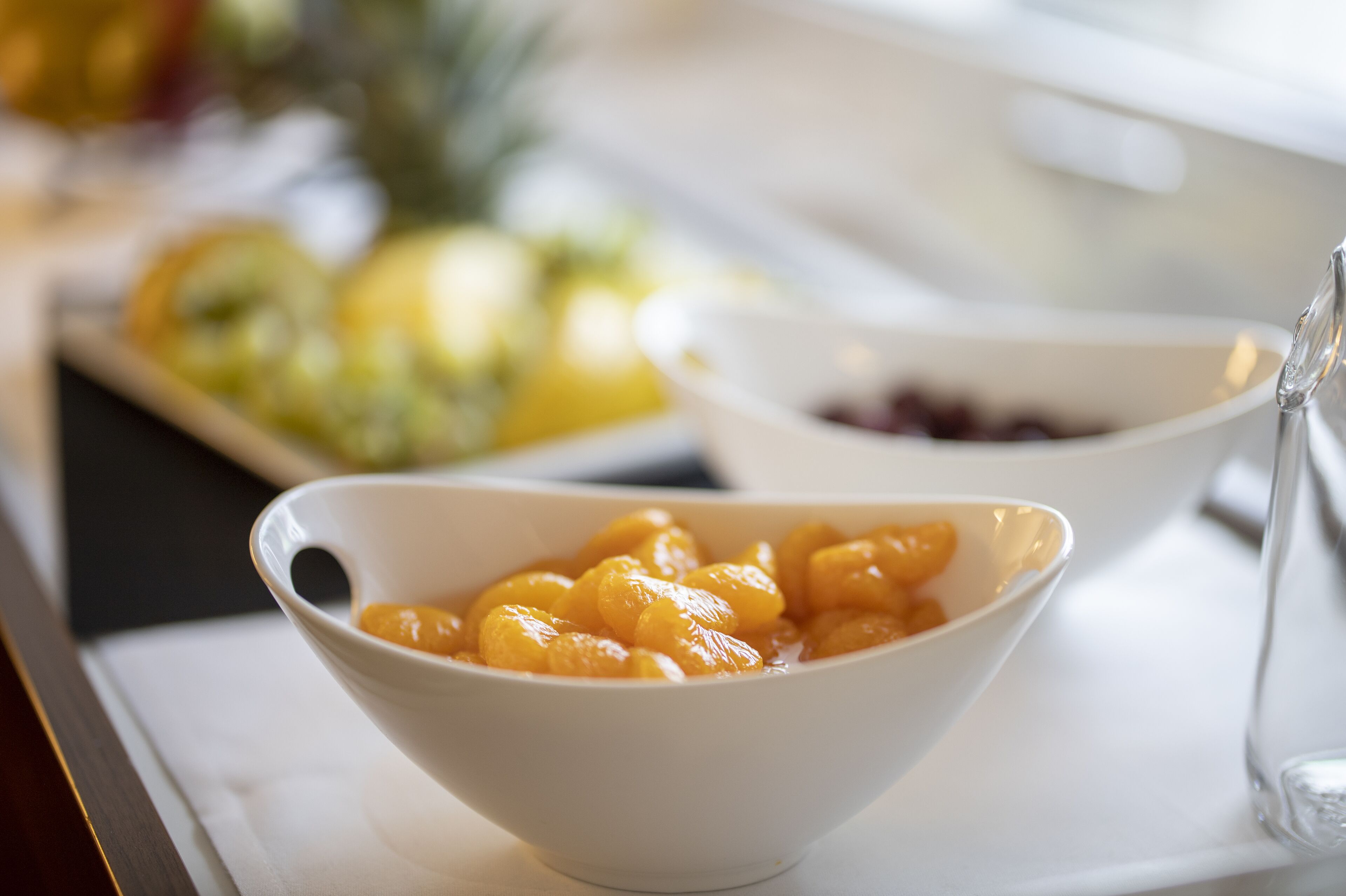 A white bowl filled with fruit, placed on a table with a white napkin.