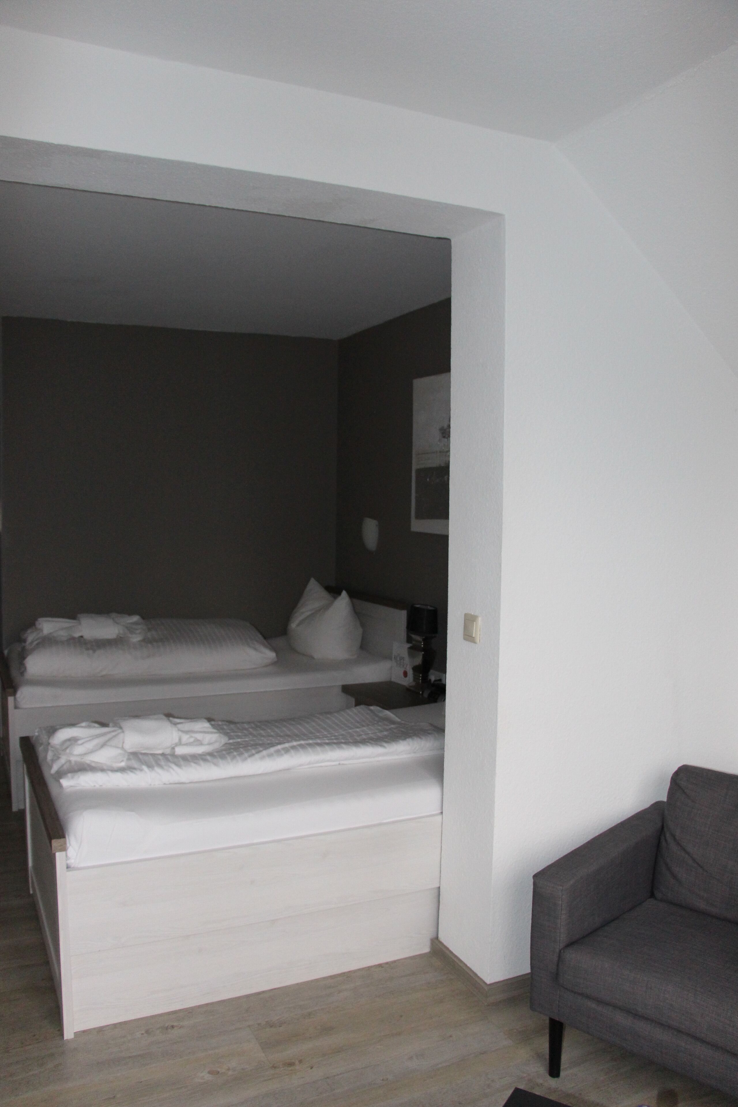 Une chambre avec deux lits, un canapé gris et un mur blanc.