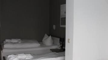 Une chambre avec deux lits, un canapé gris et un mur blanc.