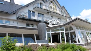 Een hotel met een modern architectonisch ontwerp, met een grote centrale pijler, balkons en een goed onderhouden tuin.
