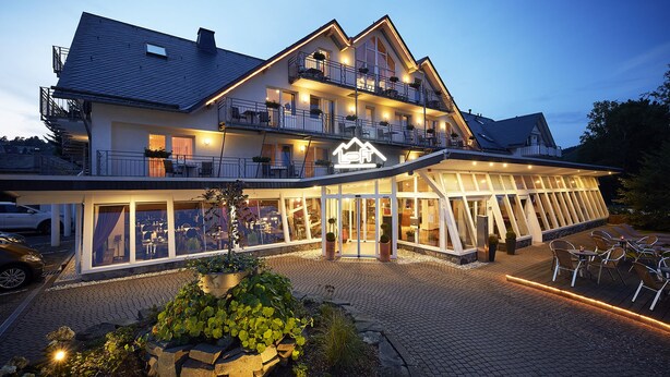 Een hotel met twee verdiepingen, een opvallende daklijn, een terras en een goed verlichte ingang.