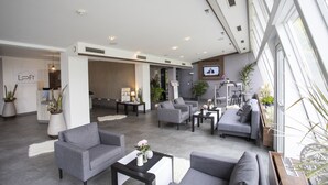 Een moderne hotel lobby met grijze banken, een receptiebalie en potplanten.