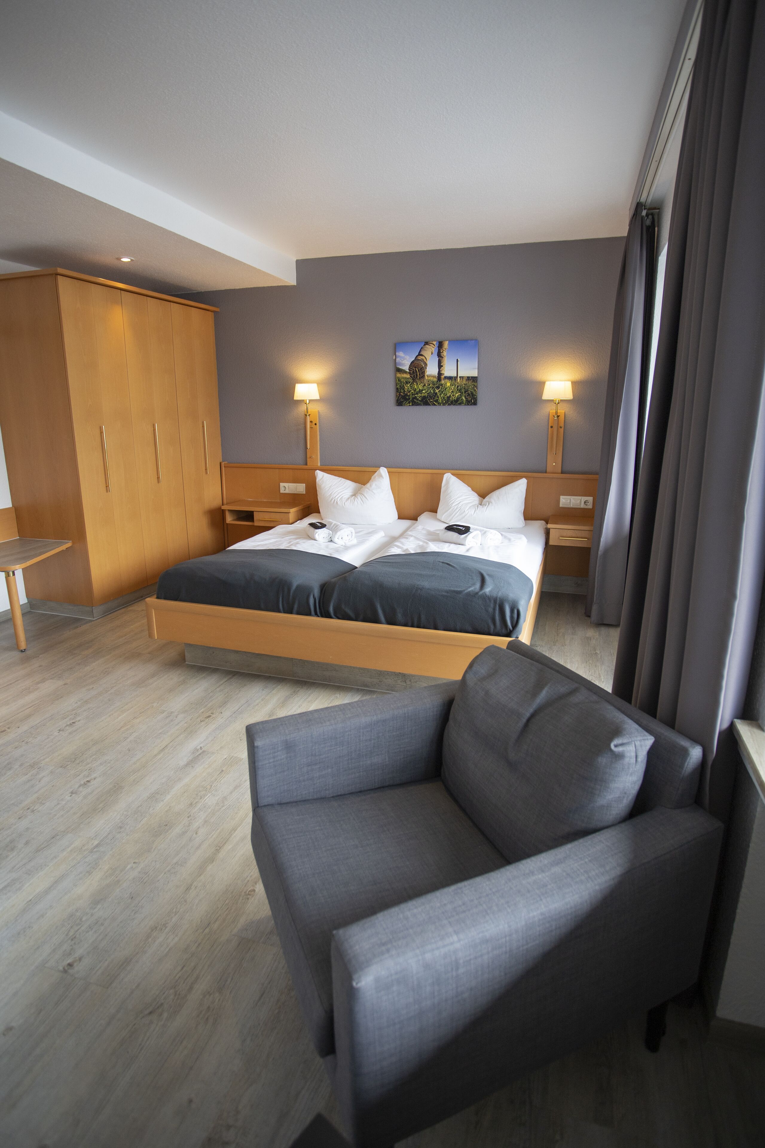 A hotel room with a bed, a chair, a wardrobe, and two bedside lamps.
