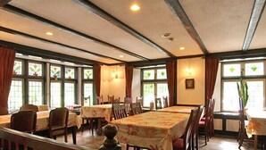 Un comedor con varias mesas y sillas, amplias ventanas con vidrieras y vigas de madera en el techo.