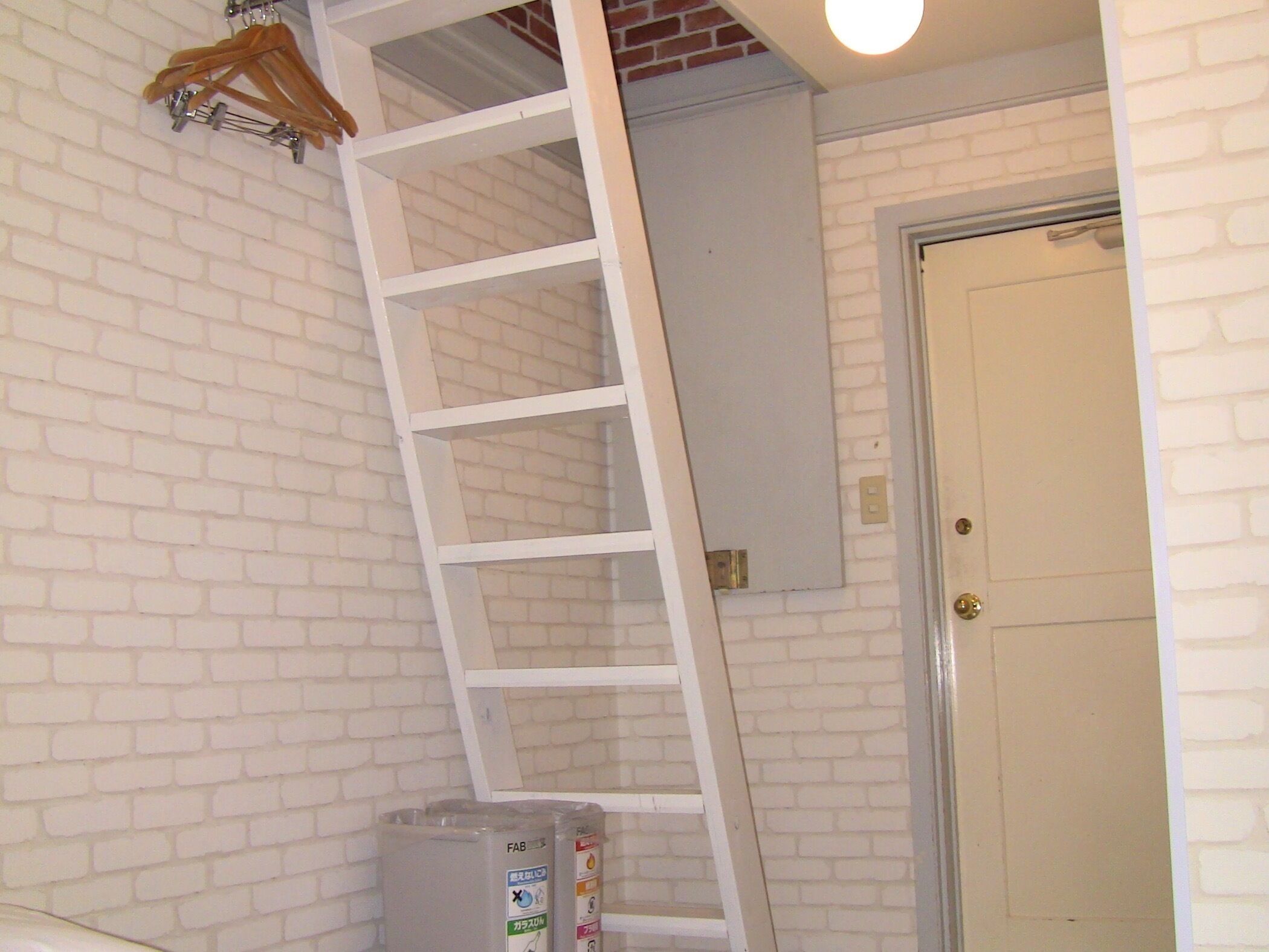 A room with a white brick wall, a white door, and a white ladder leaning against the wall.