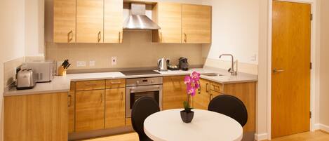 Una cocina moderna con armarios de madera, una campana extractora de acero inoxidable, un tostador, una cafetera y una mesa con sillas.