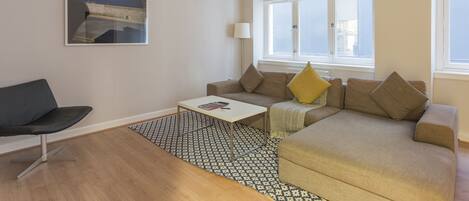 Un salon moderne avec un canapé, une table basse et un fauteuil. Il y a une fenêtre avec des stores, une lampe et un tableau au mur.