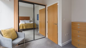 Una habitación de hotel moderna con una cama, una silla, un aparador y una puerta corredera que da a otra habitación.