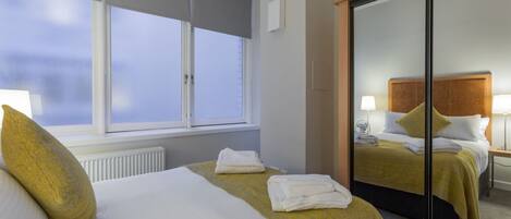 A hotel room with two beds, a large mirror, a radiator, and a window with blinds.