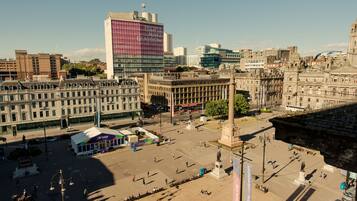 Uma praça urbana com um monumento, edifícios e um amplo edifício moderno com fachada rosa e branca.