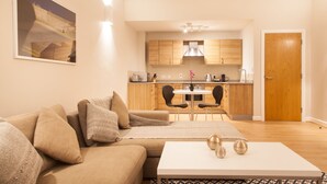 Una sala de estar moderna con un sofá color beige, una mesa de centro blanca y una zona de comedor con una mesa redonda y sillas.