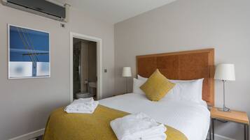 A hotel room with a large bed, two bedside lamps, a wooden headboard, a yellow throw blanket, and a white towel on the bed.