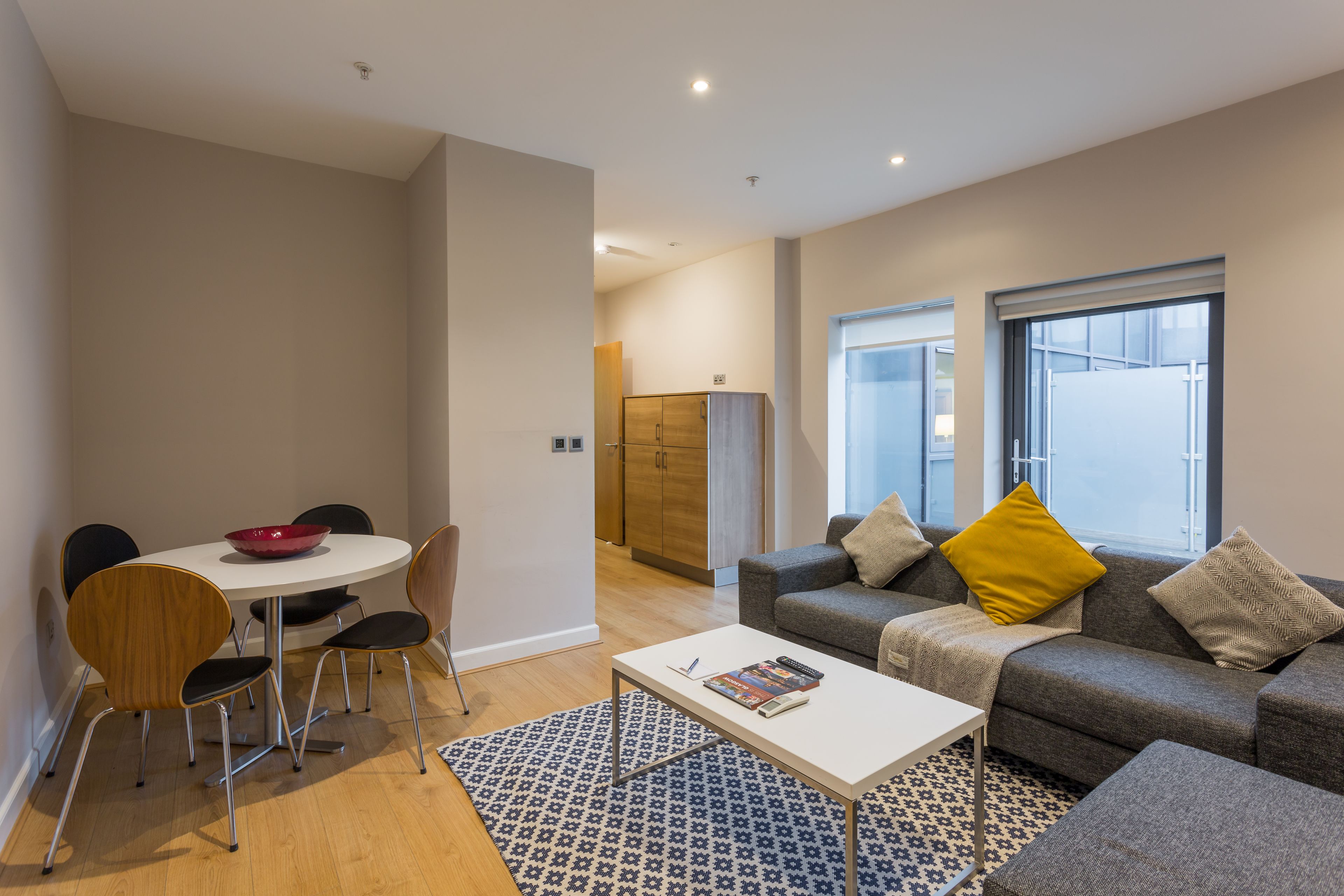 A modern living room with a grey sofa, a coffee table, a dining table with chairs, and a patterned rug.