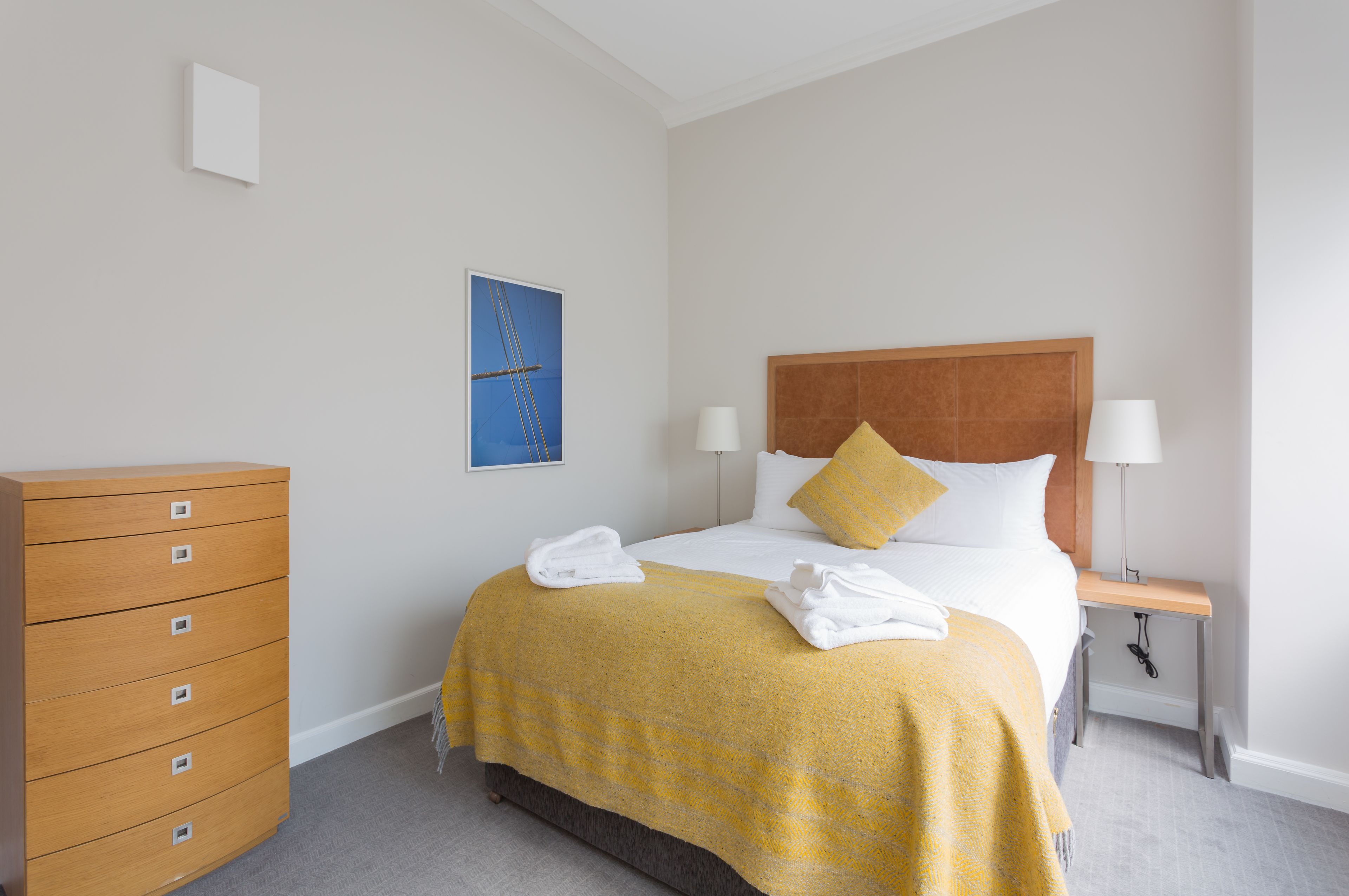 Una habitación de hotel con cama, cómoda de madera, mesita de noche y lámpara de pared.