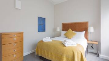 Una habitación de hotel con cama, cómoda de madera, mesita de noche y lámpara de pared.