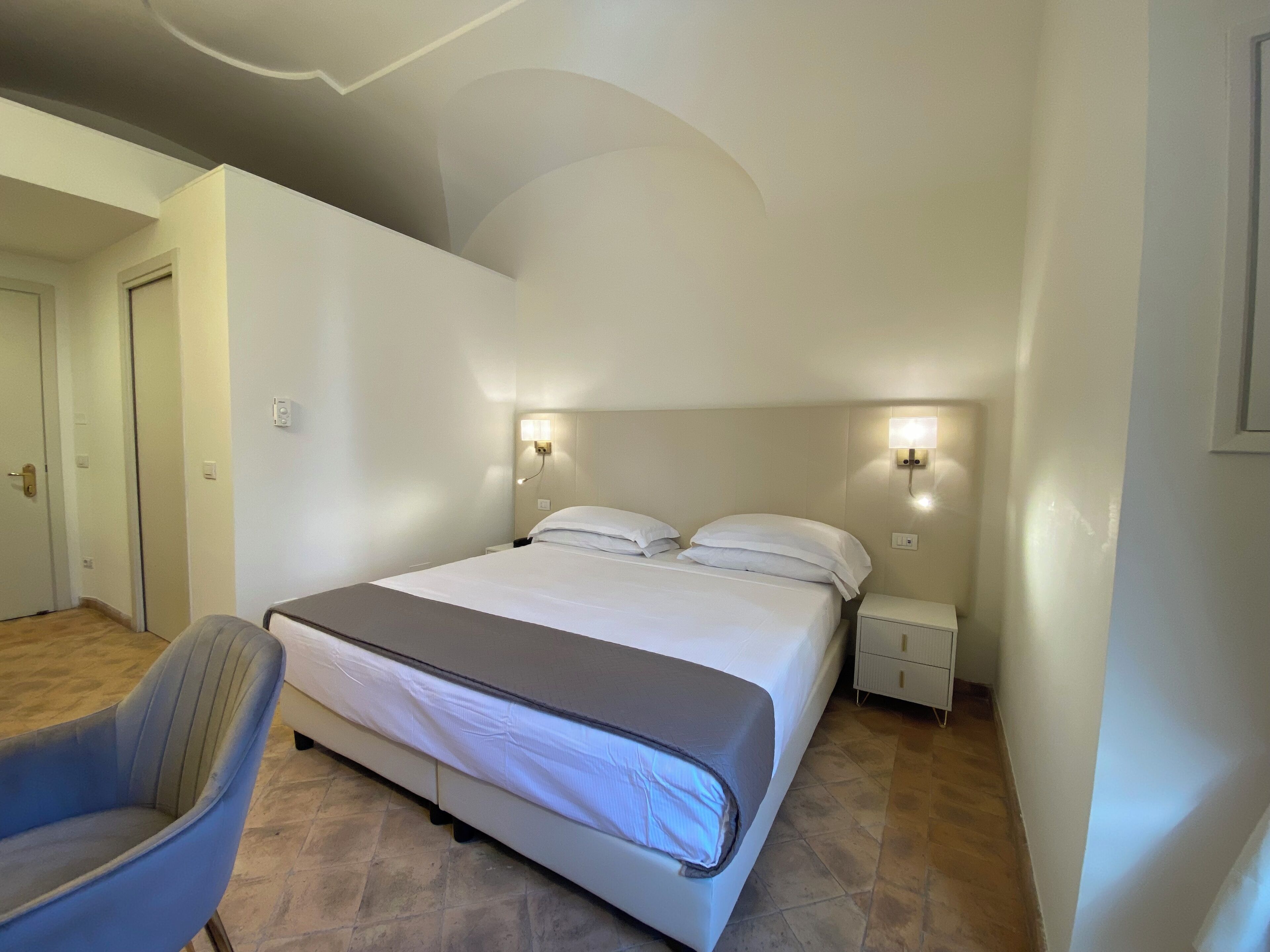 A bedroom with a bed, two bedside tables, a chair, and a door.