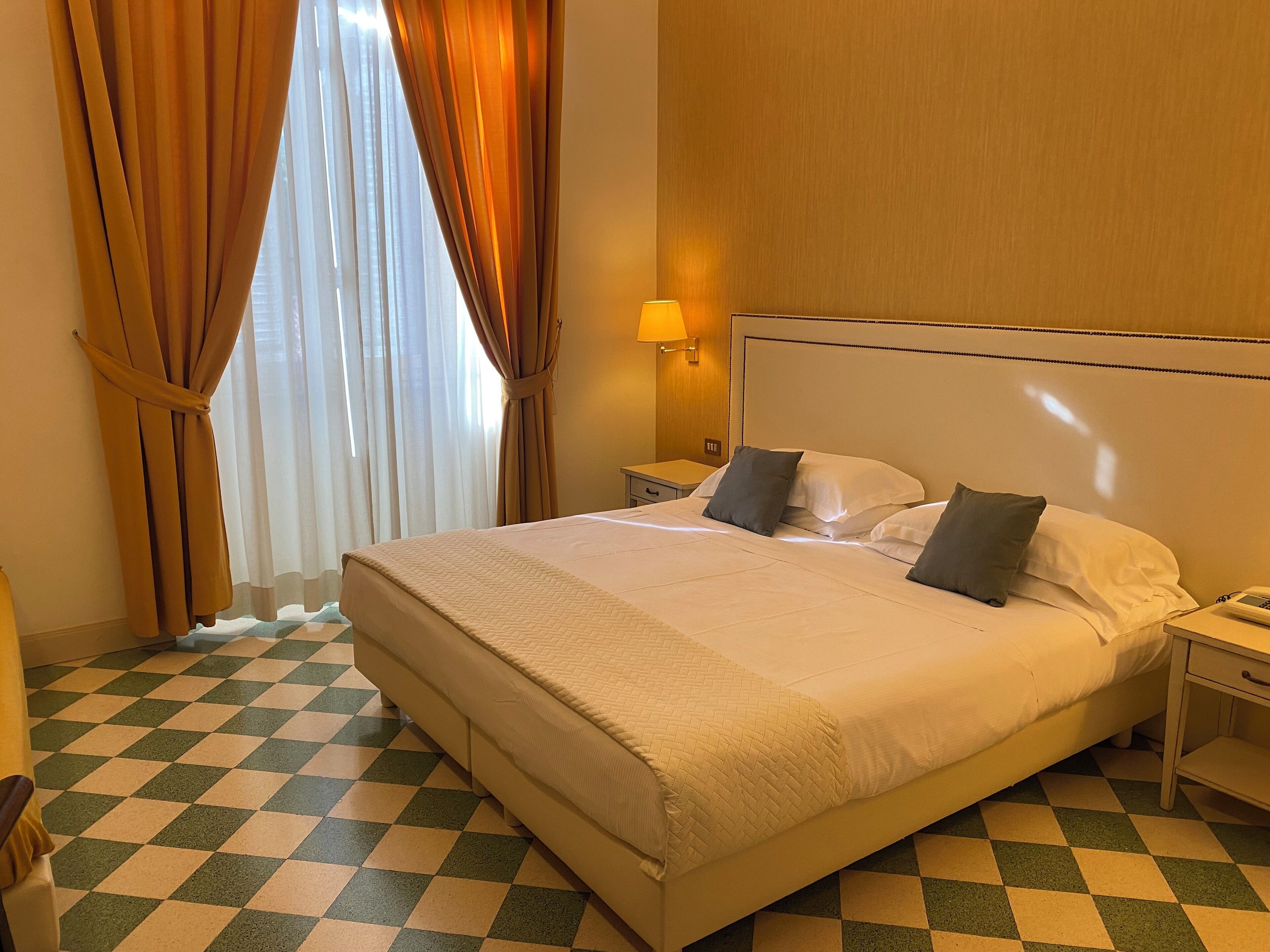 A hotel room with a large bed, a nightstand, a lamp, and a checkered floor.