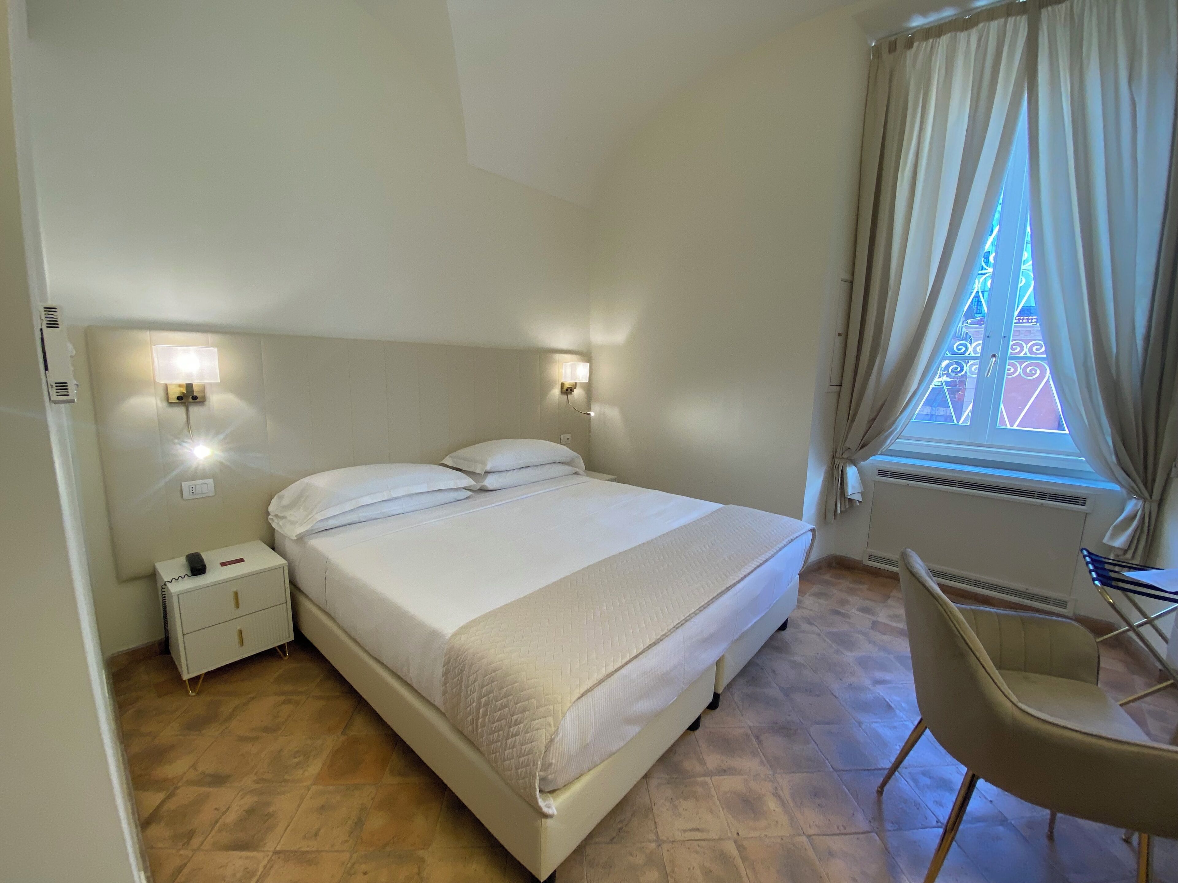 Une chambre d’hôtel avec un lit, des lampes de chevet, un bureau et une fenêtre avec des rideaux.