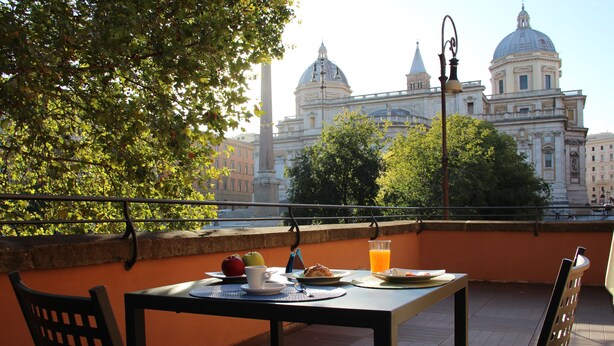 Una terraza con una mesa lista para el desayuno, con vista a un edificio histórico con cúpulas.