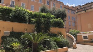 Un edificio de varios pisos con balcones, una escalera y abundante vegetación.