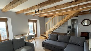 Una sala de estar moderna con una escalera de madera, sofás grises y un comedor con luz natural.