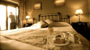 Una cama bien hecha con ropa de cama floral, una mesita de noche con lámpara y una bandeja con postre y bebidas.