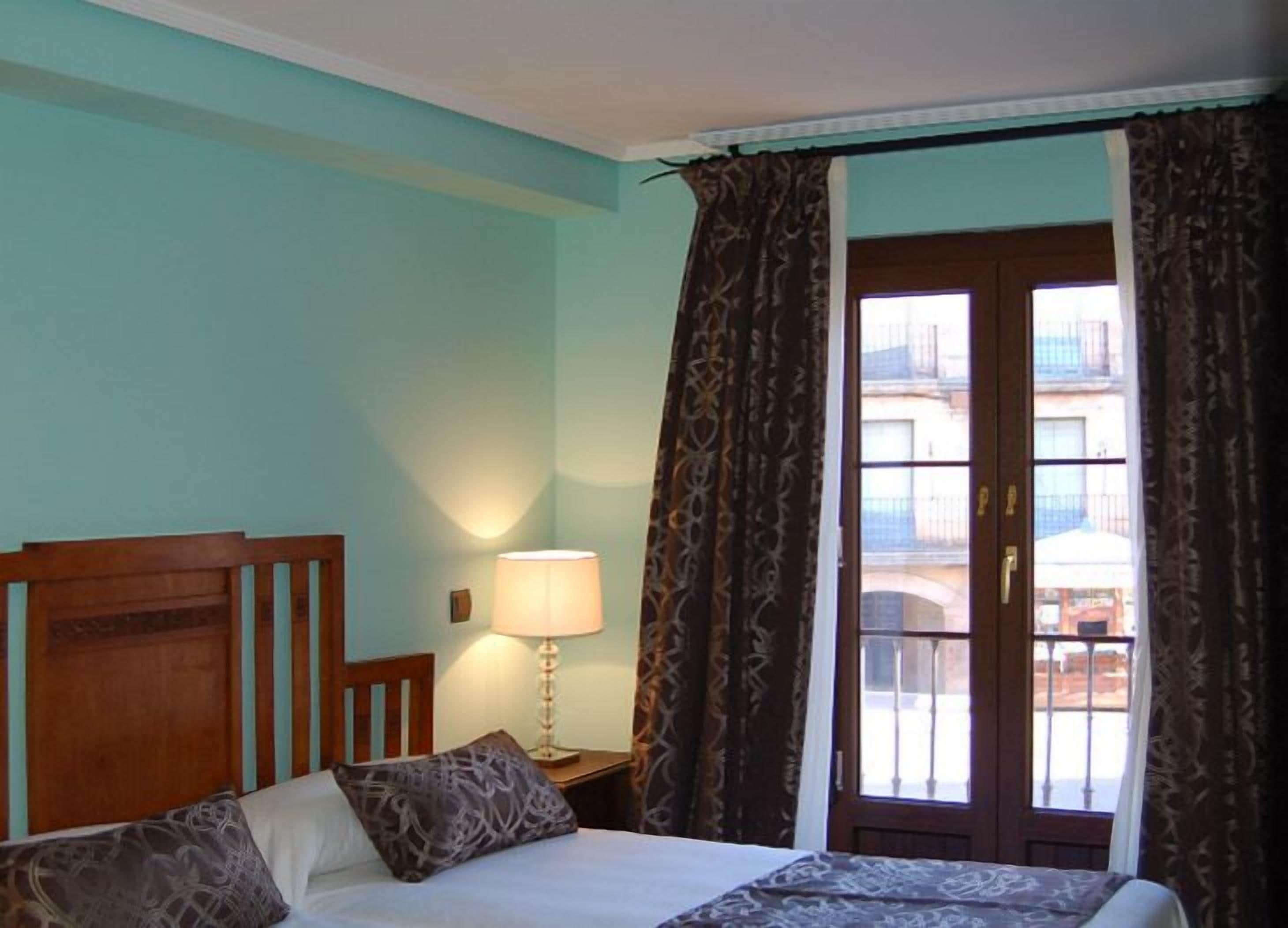 A hotel room with a bed, a bedside lamp, and a window with curtains.