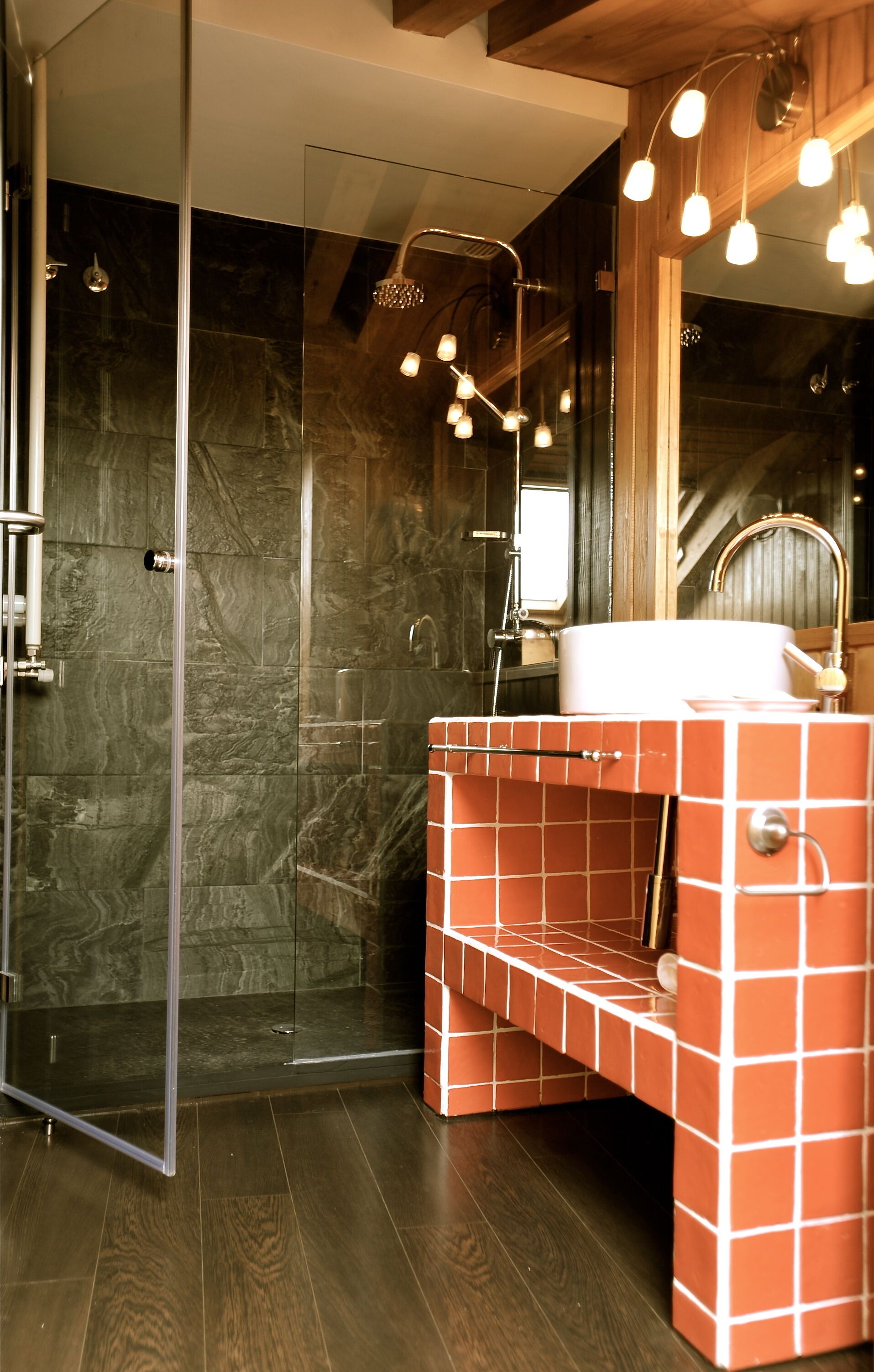 A modern bathroom with a glass shower enclosure, a red-tiled vanity, and a wooden ceiling.
