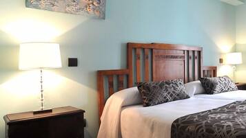 Habitación de hotel con cabecera de madera, dos mesitas de noche con lámparas, cama con ropa de cama estampada y un cuadro en la pared.
