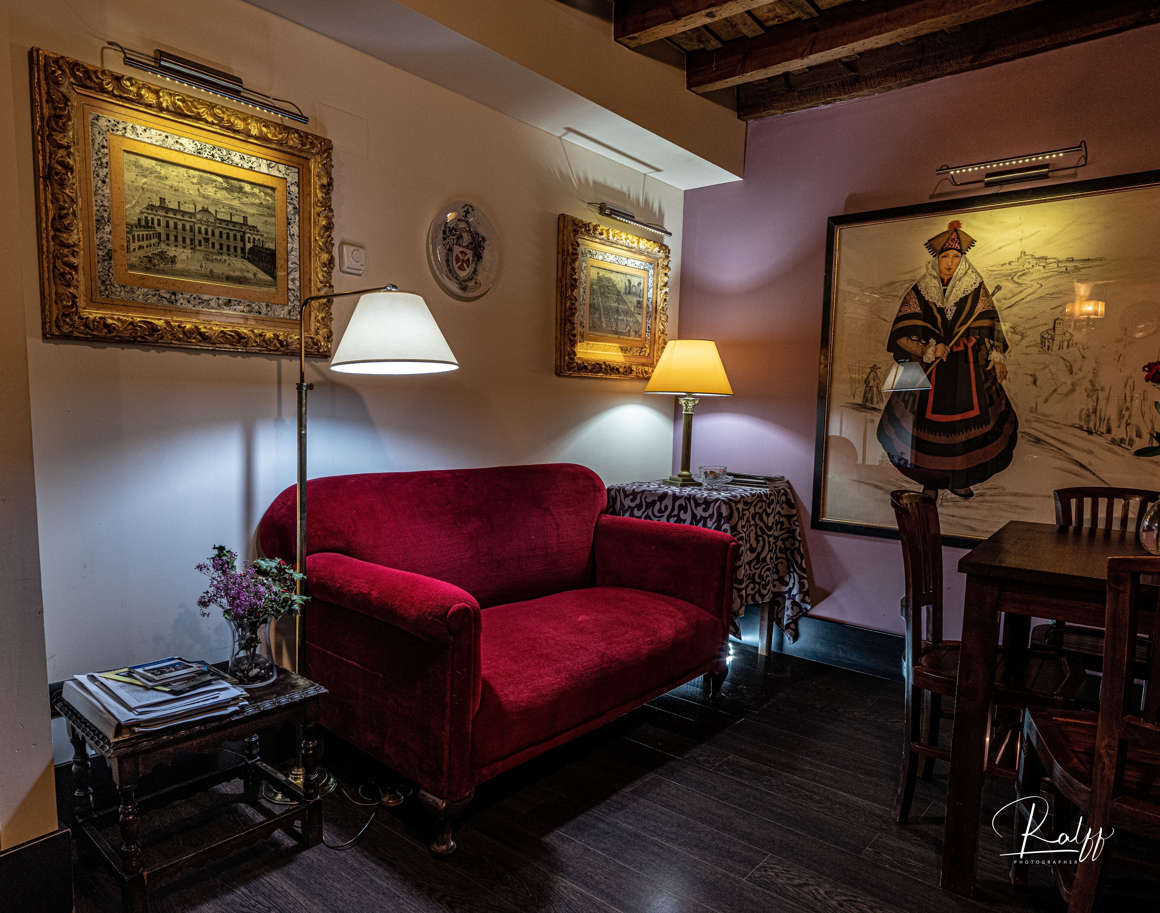 Una habitación acogedora con un sofá rojo, una mesa con lámpara y cuadros en las paredes.